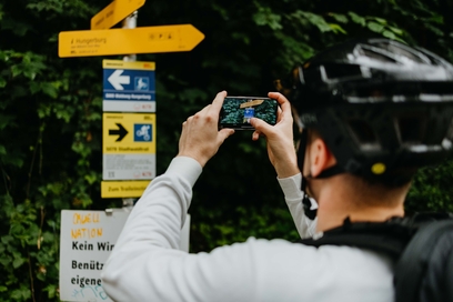 Mann mit Faradhelm und Handy fotografiert Wegweiser für Radwege ab